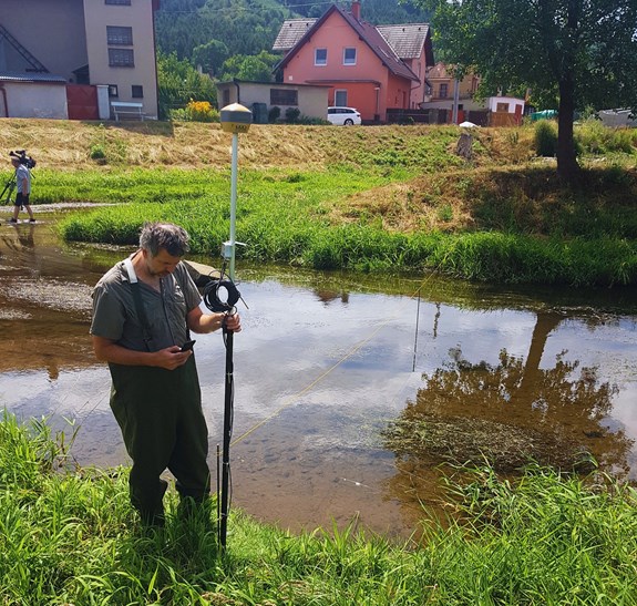 Geographer Ondřej Hájek points a high-precision GPS to measure a transect of temperatures across the Bobrůvka River in Dolní Loučky during a report on 20 July 2023. Photo: Petr Pařil