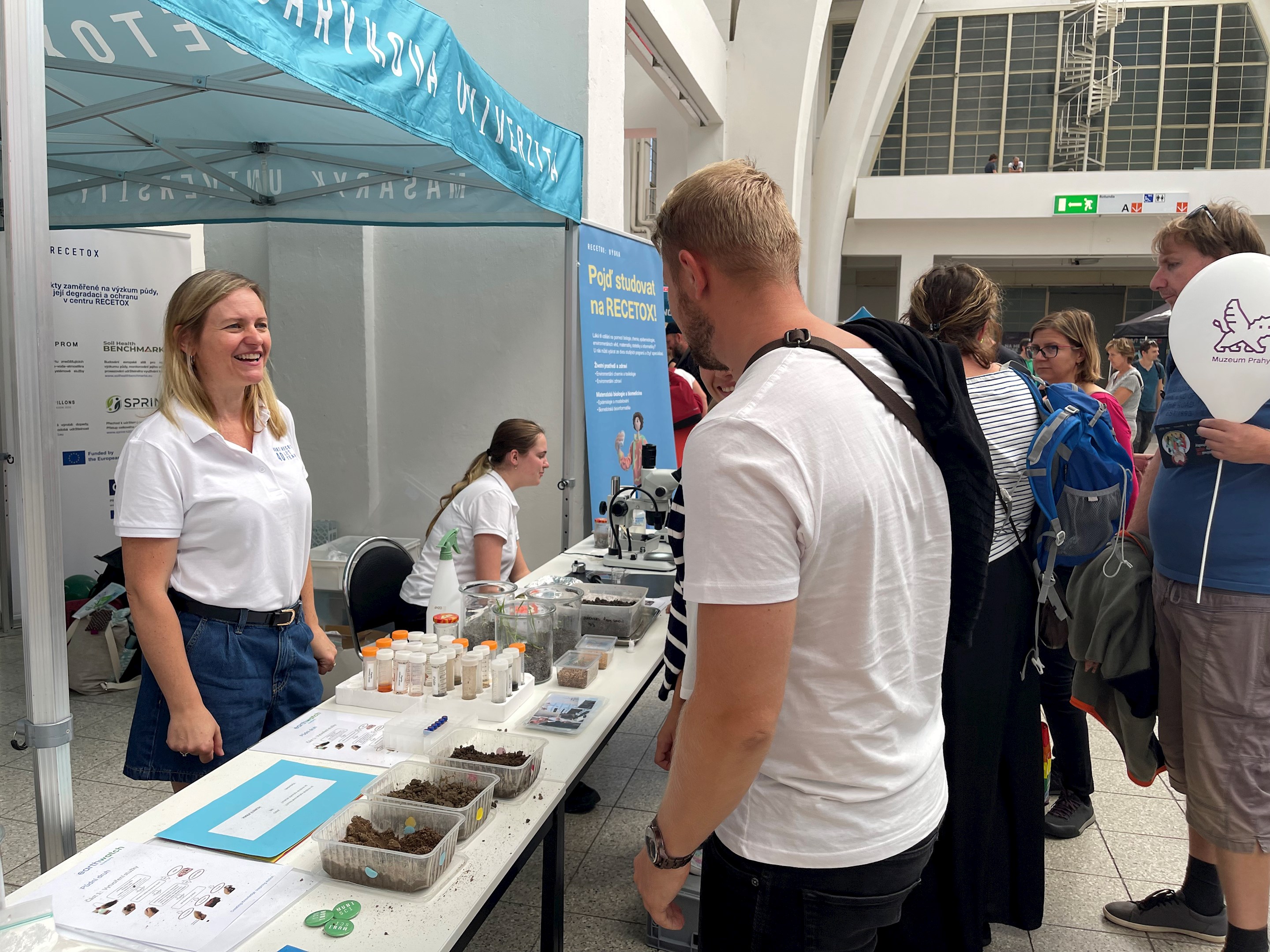 Lidé si prohlížejí stánek s vědeckými a vzdělávacími exponáty ve veřejné budově.